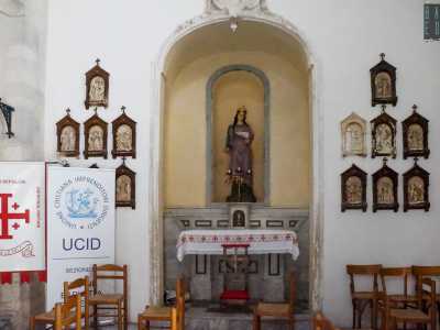 Di fronte a noi osserviamo una delle decorazioni sopravvissute: una statua di Santa Lucia posta su un altare in marmo, racchiusa in una nicchia in pietra e circondata da cornicette in legno con le tappe della Via crucis